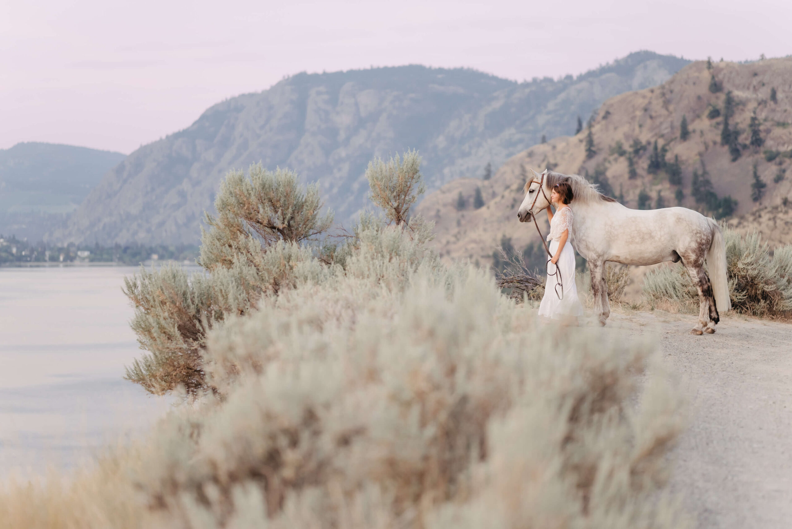 girl sits in grey building petting her white horse