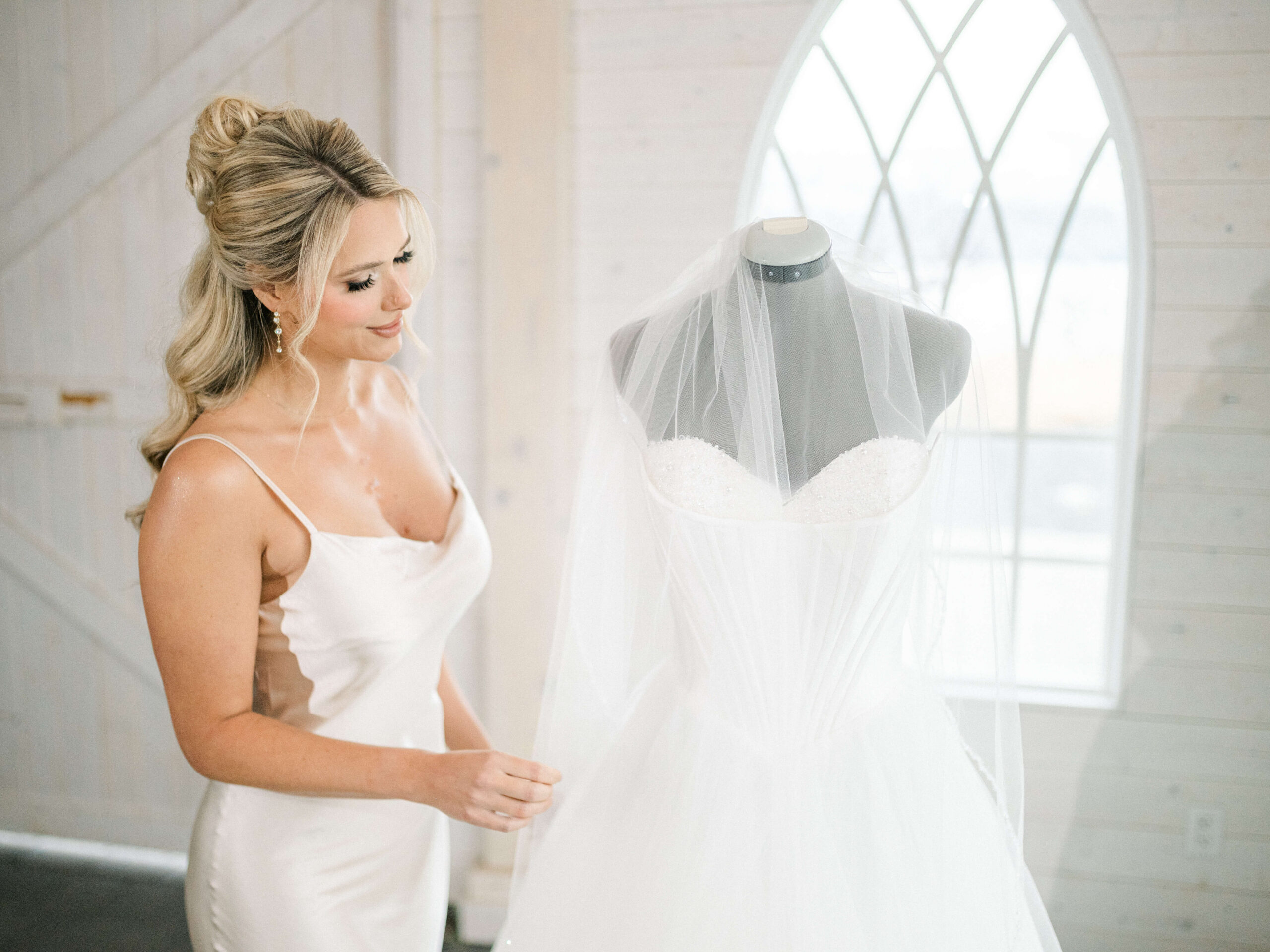 bride looks at dress with kelowna hair and makeup done