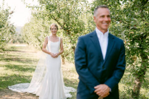 bride stands behind groom as he waits to turn around and see his bride on his wedding day for a first look