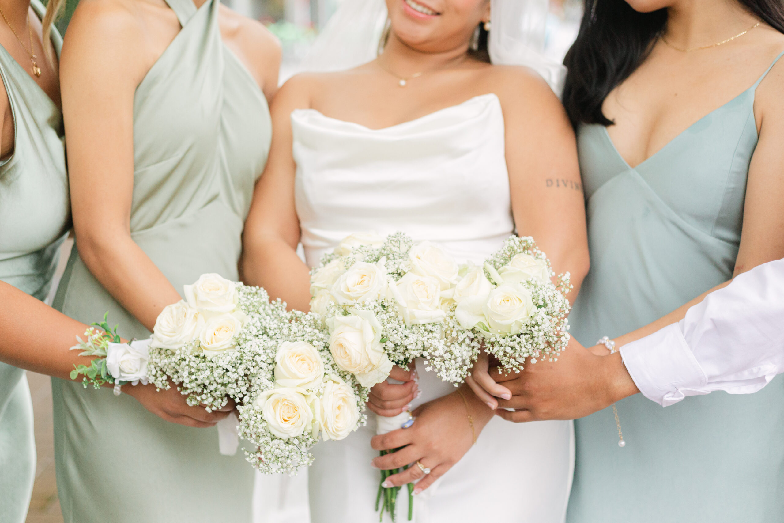 Bride and Bridesmaids hold their white rose & babys breath bouquets together. Faces are not visible.