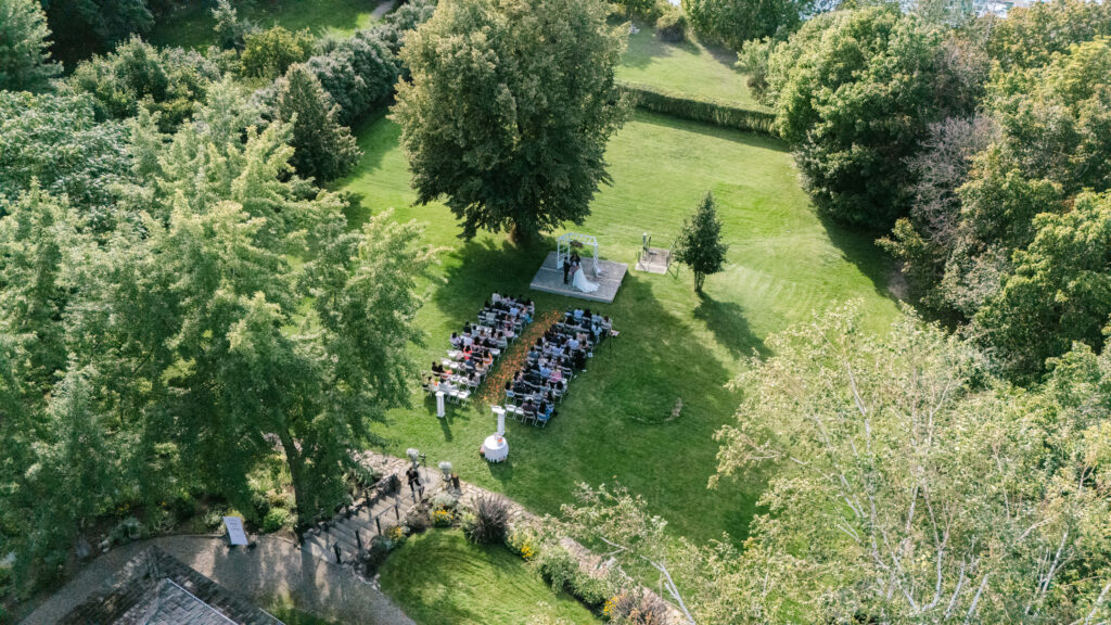 Ariel shot of the wedding ceremony of mackie lakehouse vernon wedding venue, large trees, green lawn