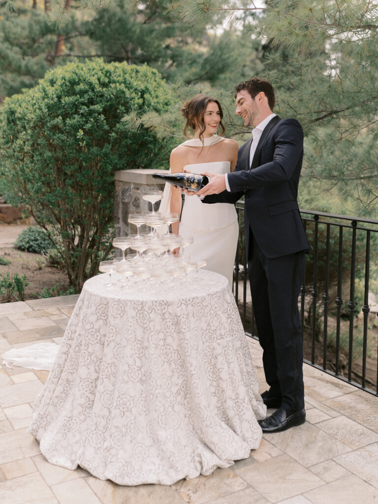 groom pours champagne at a champagne tower at a welcome dinner at a chateau okanagan wedding