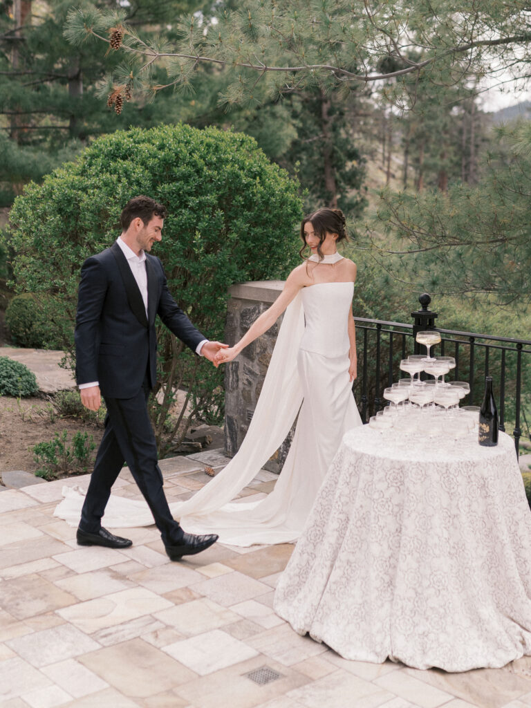 bride and groom walk toward champagne tower champagne tower at a welcome dinner at a chateau okanagan wedding